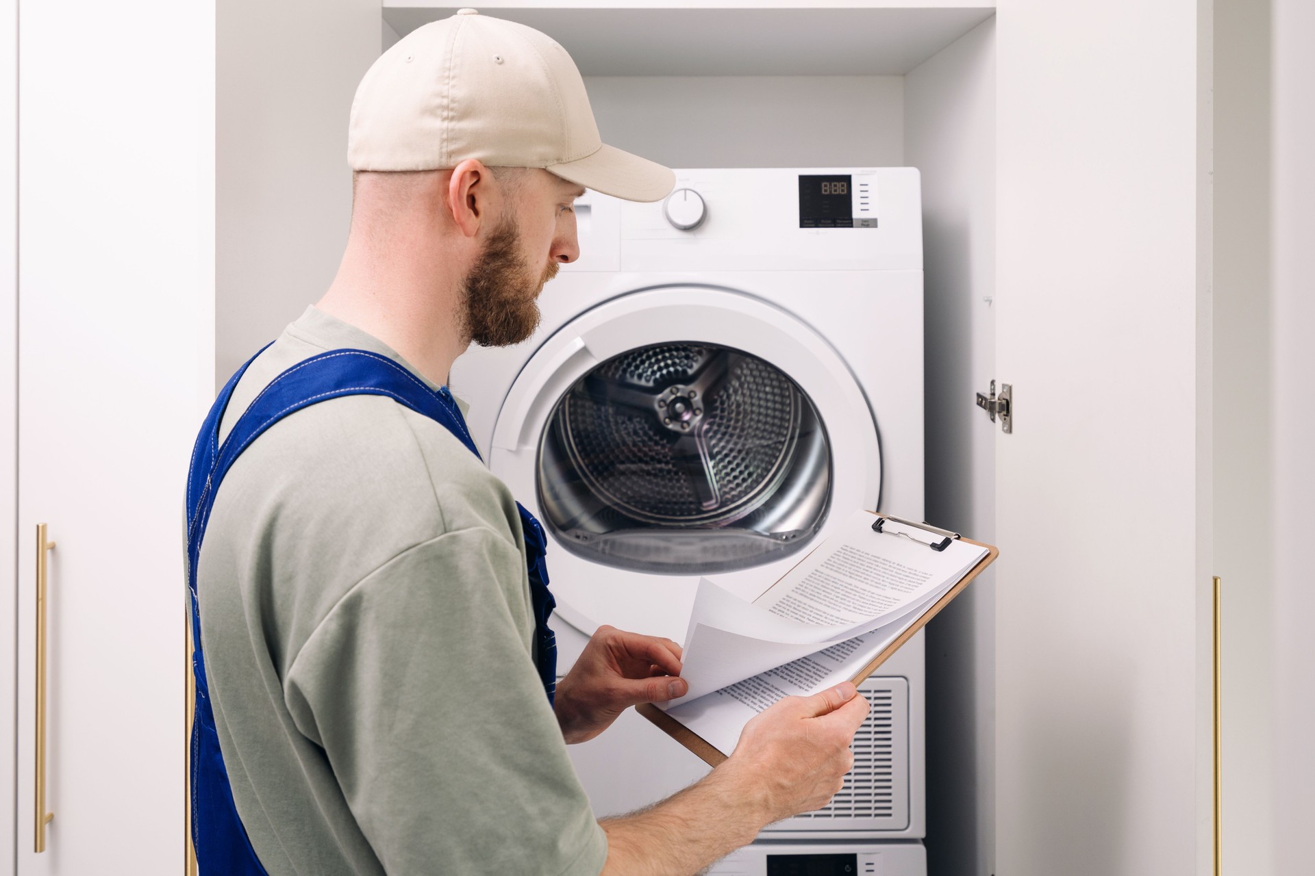 A technician inspects a washing machine while checking notes in a modern laundry room